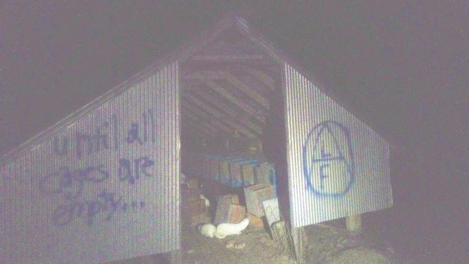 Shed with opened mink cages, tagged with graffiti reading "until all cages are empty..." and an ALF logo