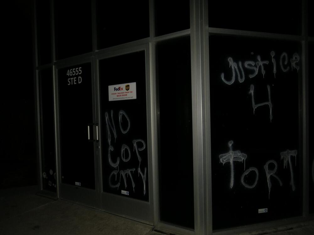 Office building windows, vandalized with acid-etching paint, read "No Cop City" and "Justice 4 Tort"