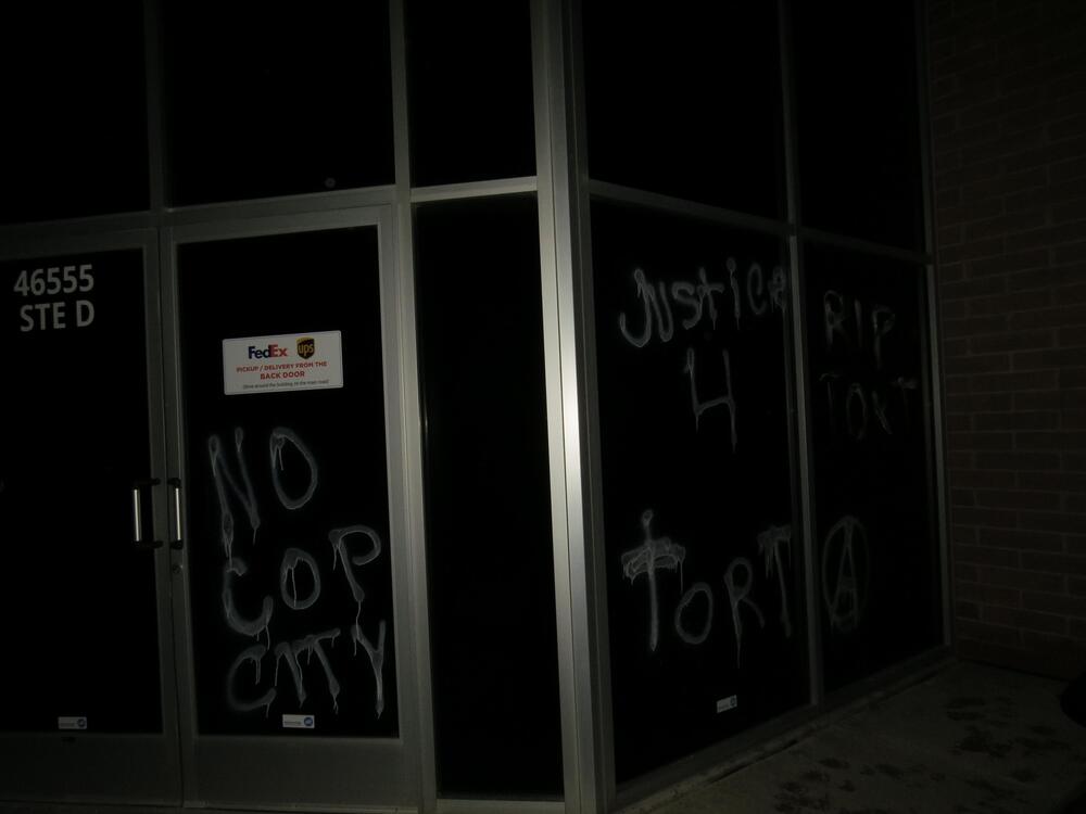 Office building windows, vandalized with acid-etching paint, read "No Cop City", "Justice 4 Tort", "RIP TORT" and have a circle-a