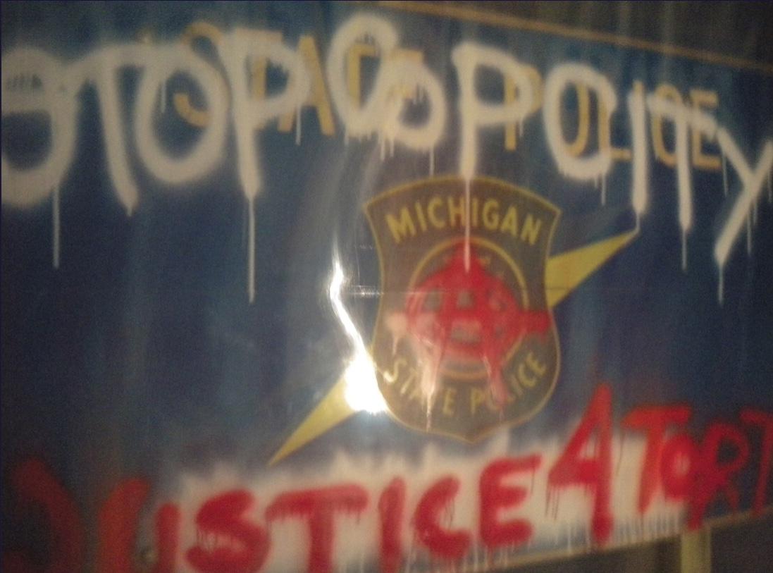Michigan State Police car with "Stop Cop City" and "Justice 4 Tort" written on it with spray paint, with a circle-a over the Michigan State Police logo