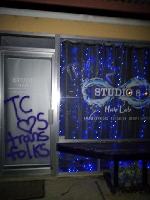 The storefront of a salon whose owner made transphobic comments is vandalized with spraypaint reading "TC loves trans folks" on the door, and "Trans power" etched on the window.