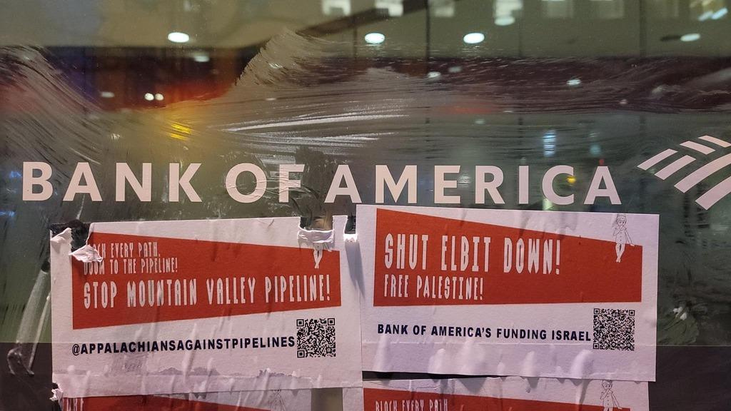 Flyers wheat-pasted to a Bank of America branch window reading "Block Every Path! Doom to the Pipeline! @appalachiansagainstpipelines" and "Shut Elbit Down! Free Palestine! Bank of America's Funding Israel". Each has a QR code