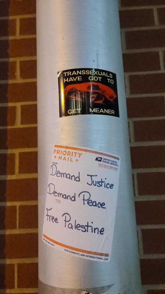 A pole with stickers reading "Transsexuals Have Got To Get Meaner" and "Demand Justice, Demand Peace, Free Palestine"