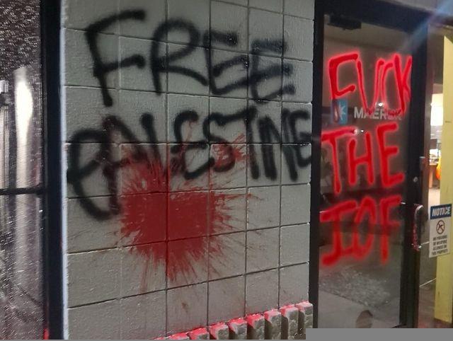 "FREE PALESTINE" and "FUCK THE IOF" are written on the exterior wall and door of a MAERSK office, with a large red paint splatter on the wall.