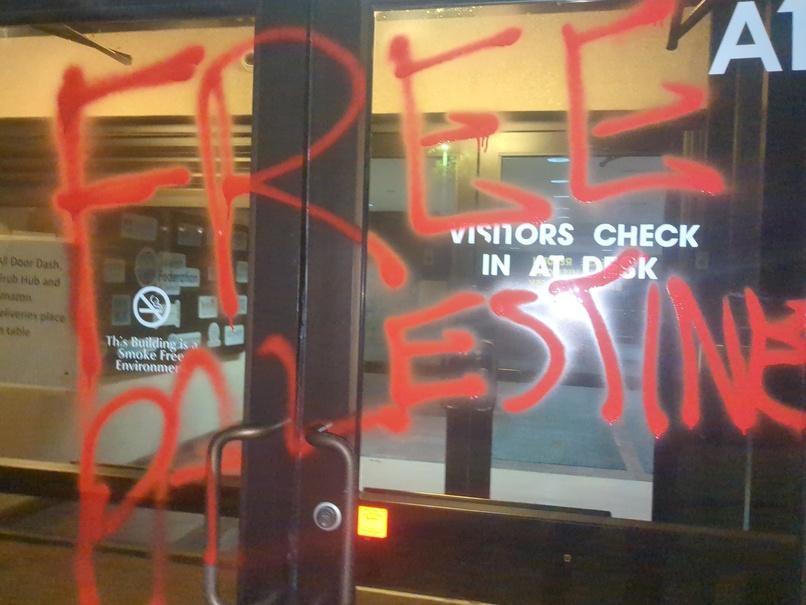 The front doors of an office building are spray-painted with "Free Palestine"