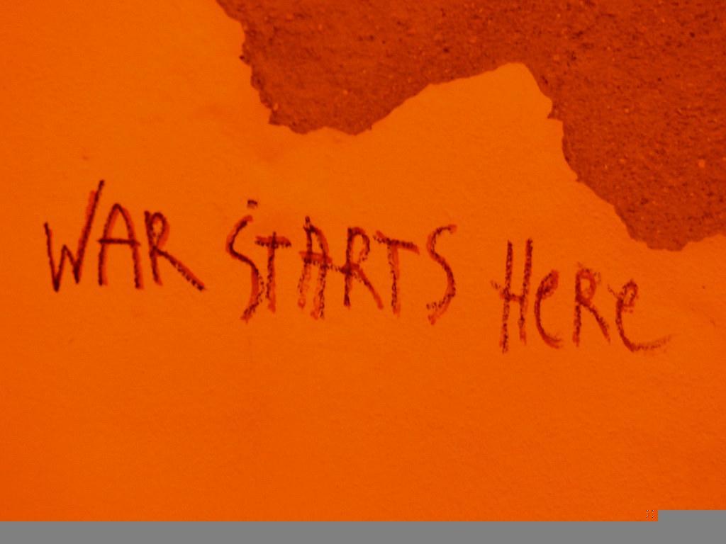 Graffiti on a wall reads "war starts here"