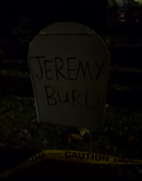 A prop gravestone in a lawn that reads "Jeremy Burd"